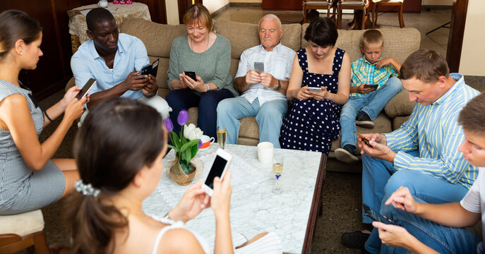 Large multiracial family sitting with mobile gadgets in cozy living room. Concept of family phubbing