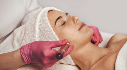 Professional beautician using derma pen on woman's face skin, at spa salon. Cosmetology and...