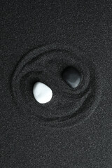 Yin Yang symbol made with stones on black sand, top view. Zen concept