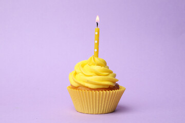 Delicious birthday cupcake with yellow cream and burning candle on violet background