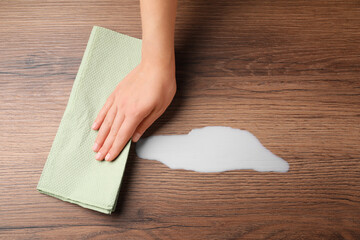 Woman wiping spilled milk with paper napkin on wooden surface, top view