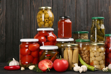 Glass jars with different pickled vegetables and mushrooms on wooden background