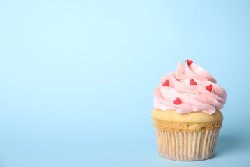 Tasty cupcake with heart shaped sprinkles on light blue background, space for text. Valentine's Day celebration