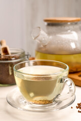 Buckwheat tea in glass cup and granules on white wooden table, closeup