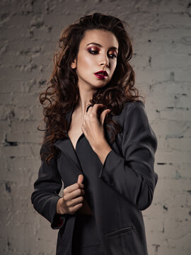 Beautiful bright makeup woman with long black curly hair style posing in silver elegant dress suit, burgundy lipstick with vamp look on grey background. Portrait
