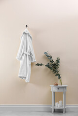 Soft comfortable bathrobe hanging on beige wall indoors