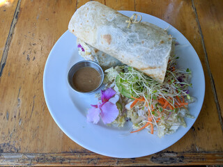 Close-up of Tofu Burrito that been cut in half with salad, dressing, and flower on a plate
