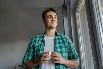 Man standing by the window with cup of coffee in morning daily routine