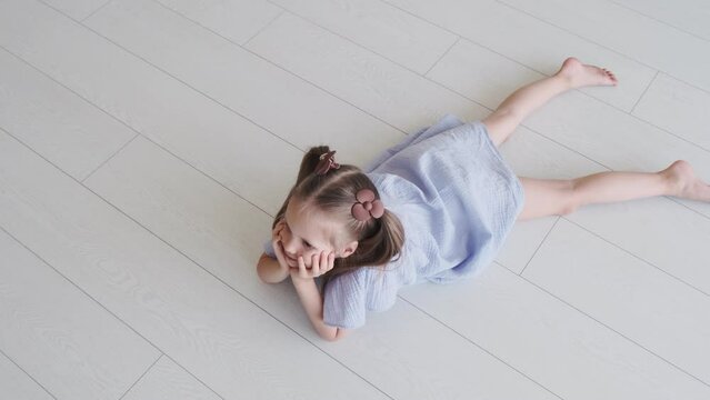 Little girl in a blue dress is lying on the floor in the bedroom. Children's products
