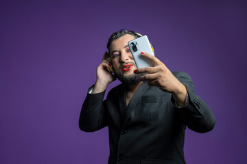 non-binary person takes selfies with his smartphone on an isolated violet velvet background