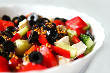 Defocus closeup summer salad. Classic Greek salad from tomatoes, cucumbers, red pepper, onion with olives, oregano and feta cheese. Fresh mixed vegetables salad in a bowl. Black olives. Out of focus