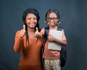 An african Nigerian mother, teacher or guardian doing thumbs up gestures with a girl child that is...