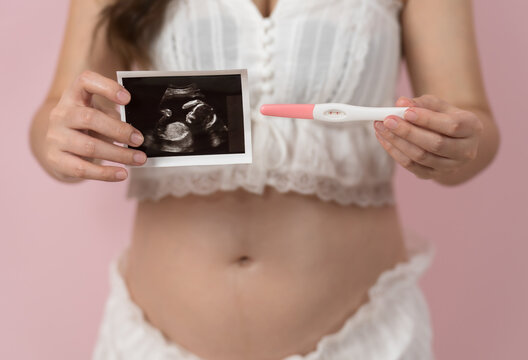 pregnant woman showing positive pregnancy test and ultrasound photo