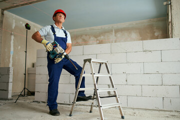 Professional construction worker in uniform standing with rotary hammer drill. Portrait of...