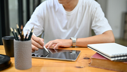 cropped image, A man in casual outfit sits at his desk using digital tablet