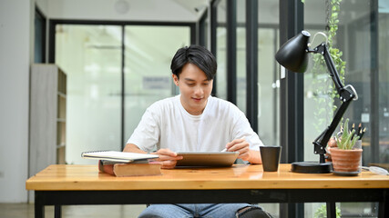 Intelligent Asian businessman working at his office desk, using his digital tablet.