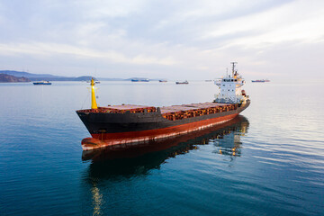 Bulk carrier ship at anchor at sunset, aerial view. Bright sunny path on water, red orange sky....