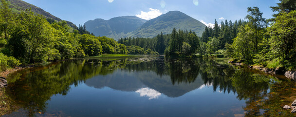 Small Scottish lake panoramic landscape,surrounded by trees at Glencoe,Scotland,United Kingdom. - obrazy, fototapety, plakaty