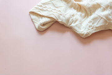 Top view of a white knitted sweater on a pink background.