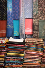 Artistic variety shade tone colors ornaments patterns, closeup view of stacked saris or sarees in display of retail shop.