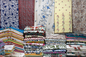 Artistic variety shade tone colors ornaments patterns, closeup view of stacked saris or sarees in display of retail shop.