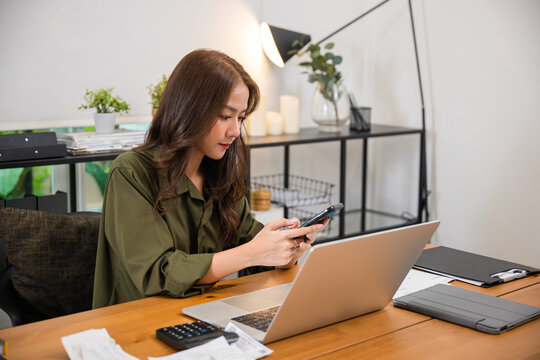 Asian Business Woman Using Laptop Checking Smartphone Indoors Home Office, Happy Female Smile Working Multiple Devices With Computer And Mobile Phone, Beautiful People Pay Digital Online On Desk