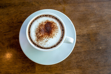 Hot chocolate or cocoa drink in a white cup, on brown wooden table.