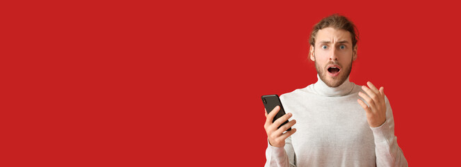 Shocked young man with mobile phone on red background with space for text