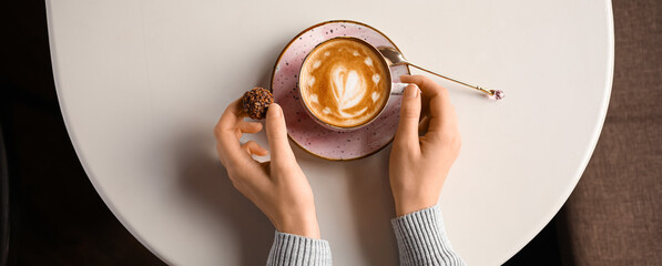 Woman with cup of coffee and candy at table, top view