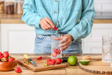 Woman preparing tasty strawberry lemonade in kitchen