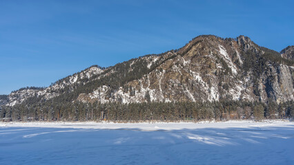 A picturesque mountain range against the blue sky. There are coniferous trees on steep rocky...