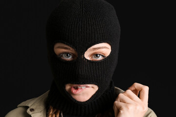 Portrait of young woman in balaclava biting lip on black background