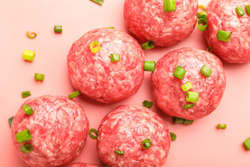 Raw meat balls with cut green onion on pink background, closeup