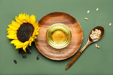 Wooden plate with bowl of oil, seeds and sunflower on color background