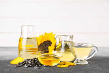 Glass containers of oil and seeds with sunflower on black and white background
