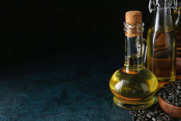 Fototapeta na wymiar Jug of oil and bowl with sunflower seeds on dark background