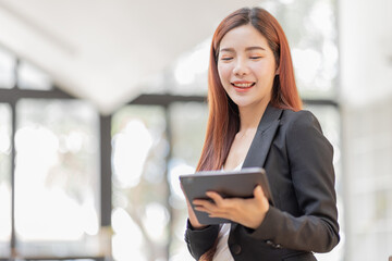 Business Asian Female holding tablet laptop and steanding in the workplace, concept of business accounting documents planning finance analysis and report,	