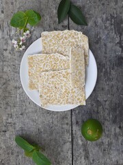 Raw tempeh, raw soybean cake from Indonesia on a plate on wooden background.