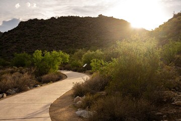Winding path through desert background and sun setting over the mountains