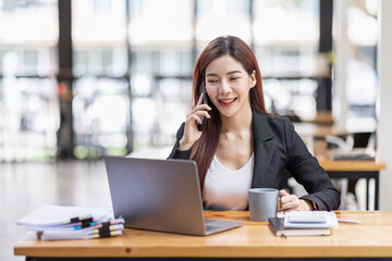 Fototapeta na wymiar Young Business Asian woman talking on a smartphone and sitting on desk in workplace, Asian female Business accountant Documents data sitting at his workplace.