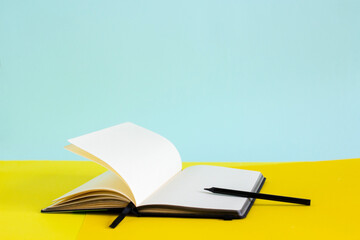 Open blank notebook and black pencil on yellow and blue background
