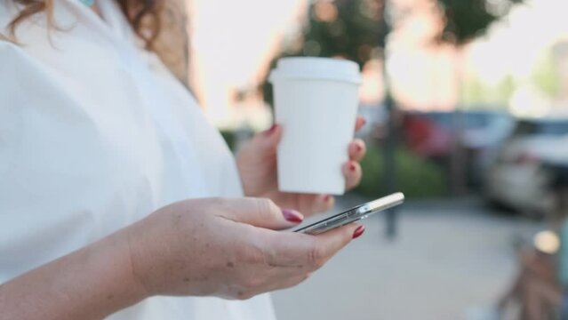 Closeup woman typing by mobile phone outdoors. Walking with smartphone in urban background.