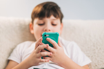 Boy playing mobile game on smartphone on sofa. Preschooler playing mobile phone. Kid using phone for gaming. Child playing video game at home. Communication and chat device