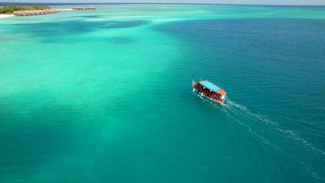 Aerial view of Maldives Dhoni boat movie across bay to island with overwater bungalows
