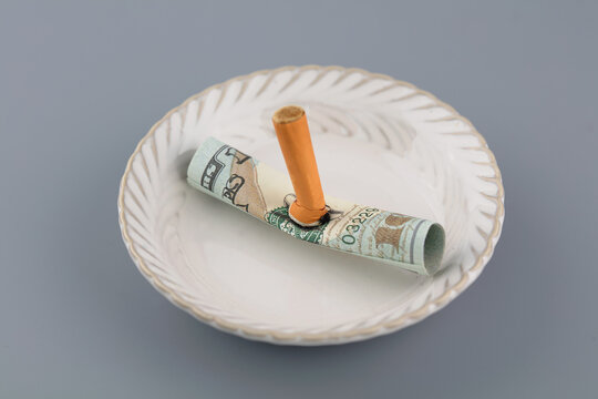 Extinguishing cigarettes on a plate on dollar bills