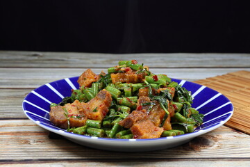 Traditional spicy fried green long bean and roasted crispy pork dressing with red chilly paste serving on the plate. Famous street food menu in Asian restaurant. 