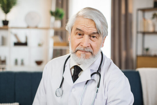 Senior grey hair caucasian male physician with a stethoscope on his shoulders sitting on sofa on the background of light conference room in hospital.