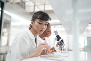 Young scientist in white lab coat working with binocular microscope in the material science lab