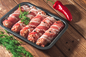 Raw lula kebab wrapped in bacon in a plate on a vintage table with dill and pepper. Free space for advertising.