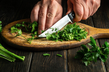 Cook cuts green parsley on a cutting board with a knife for cooking vegetarian food